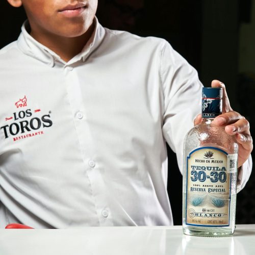 A bartender in Los Toros Restaurant displaying a bottle of Tequila 30-30, Reserva Especial.